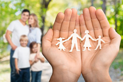 Zwei Handflächen aneinander die einen Scherenschnitt von einer Familie mit zwei Kindern halten - Eine Familie im Hintergrund Familienberatung